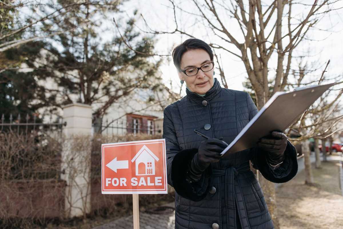 Femme examinant un document devant un panneau de vente immobilière