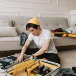 Un homme en yellow cap range des habits dans une valise ouverte